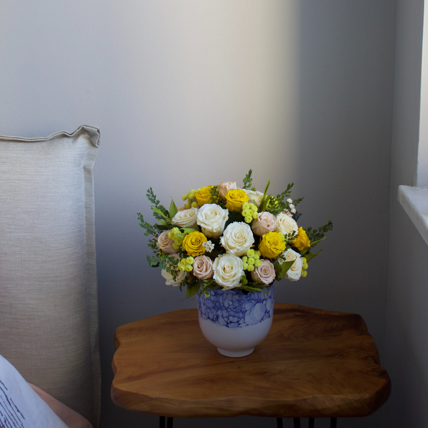 The Amalfi by Eos Blooms: preserved yellow and white roses in a blue vase on a wooden table.