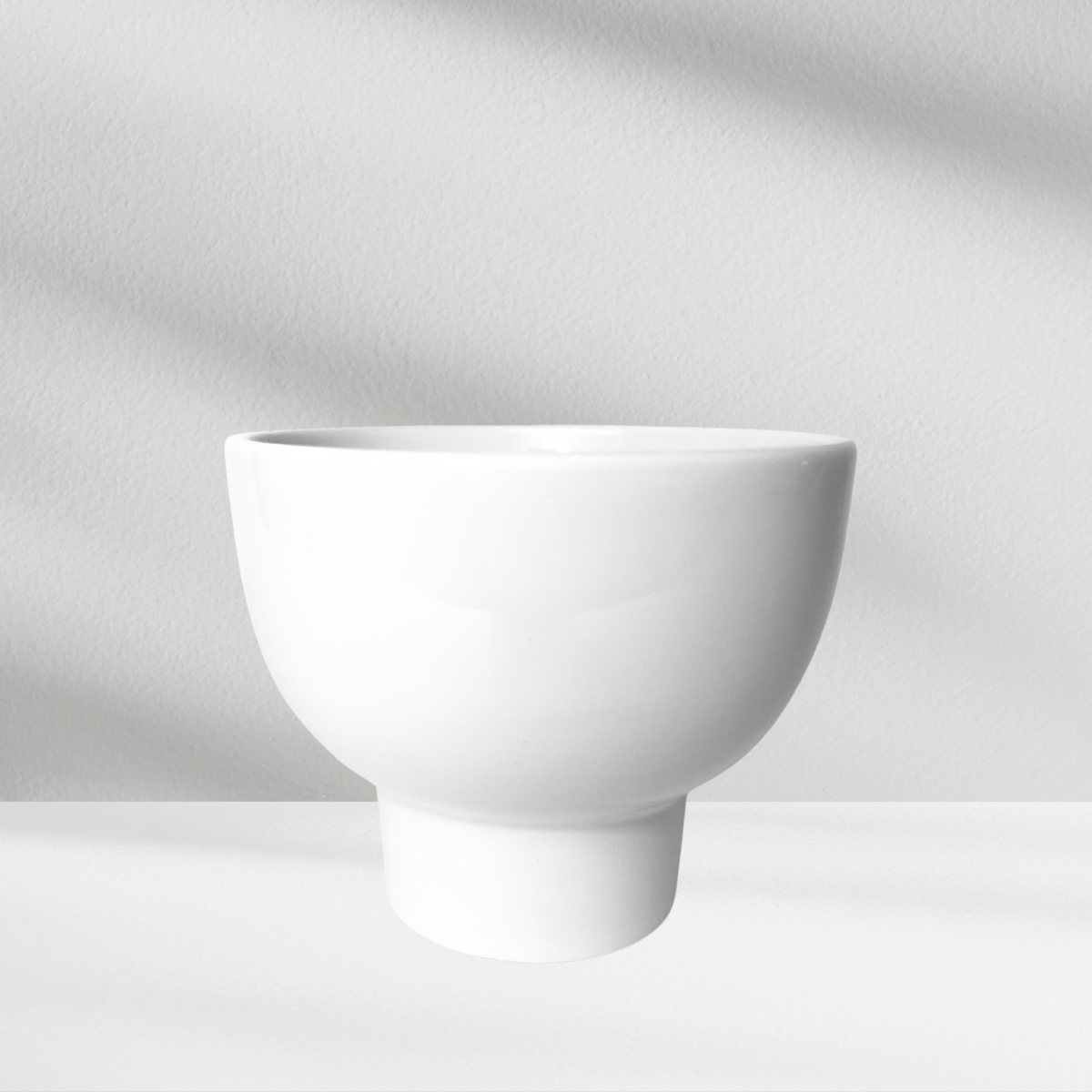 A White Pedestal by Eos Blooms displayed on a light gray textured background with a white bowl.