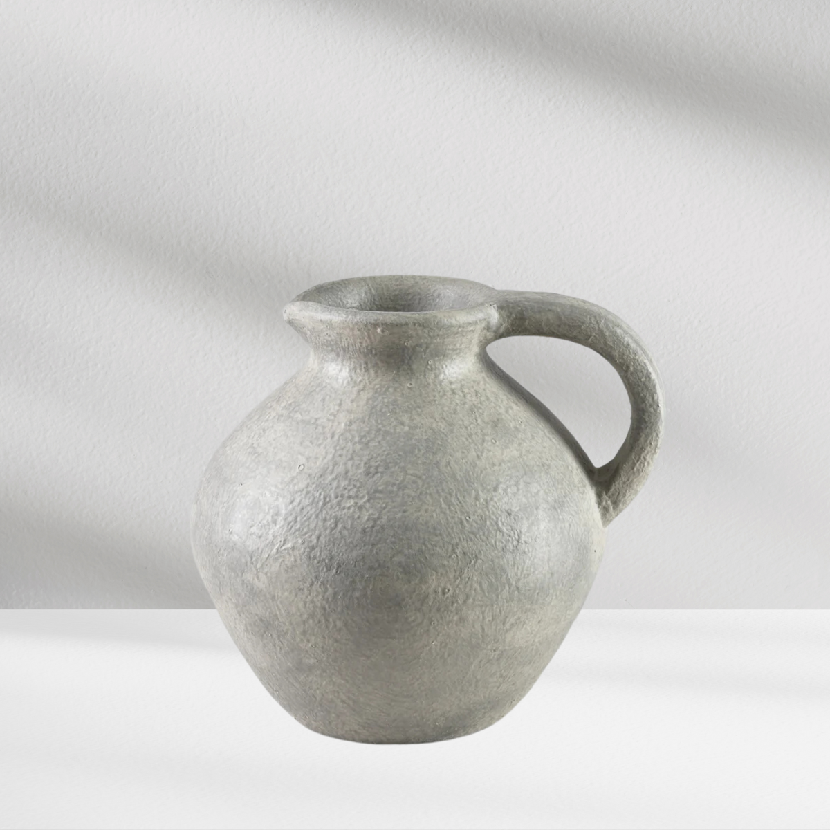 The Eos Blooms Athens Vase, textured gray with a handle, sits on a white surface.