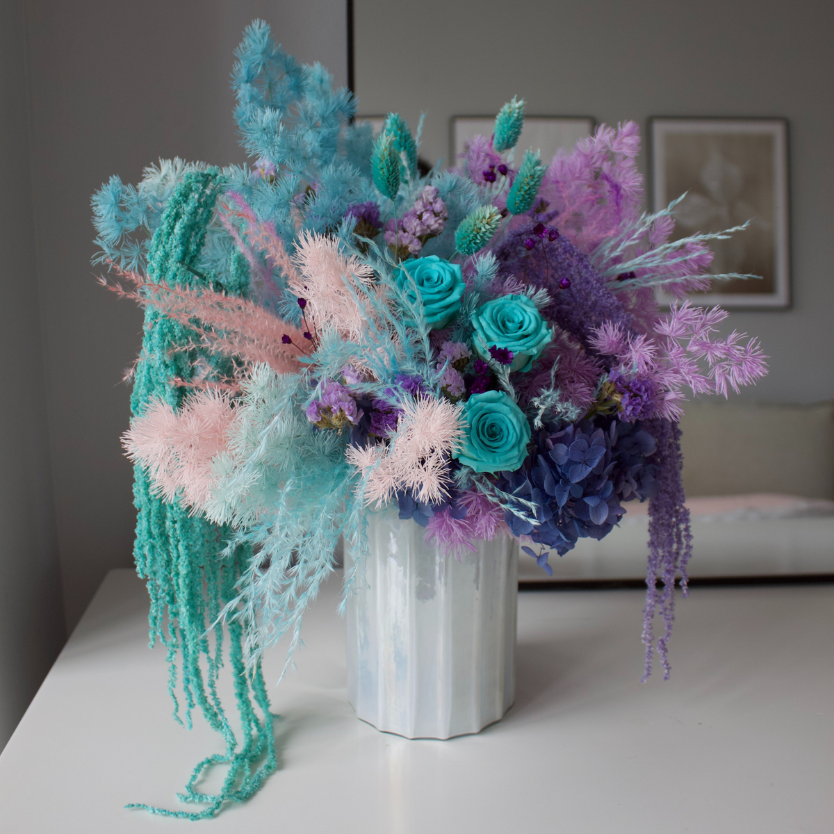 La Sirena by Eos Blooms: preserved teal, purple & pink florals in a white vase on a table.