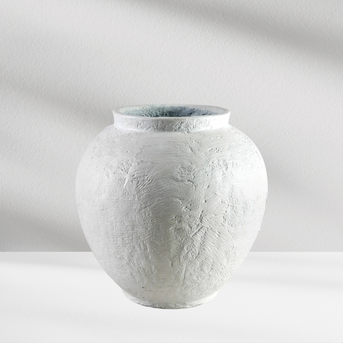 The Santorini Vase by Eos Blooms is a round, textured white ceramic piece on a white surface.