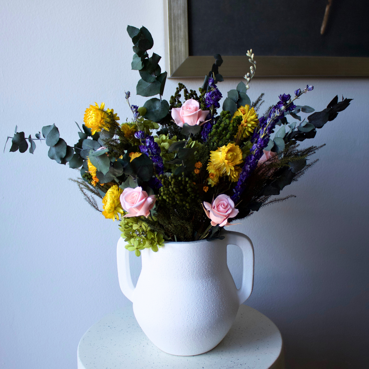 The Eos Blooms Wildbloom vase with preserved wildflowers sits on a round white table.