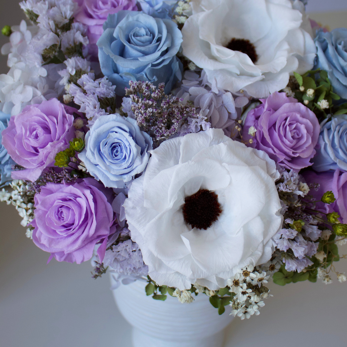 The Giverny by Eos Blooms: blue & lavender Forever Roses and white anemones in a white vase.