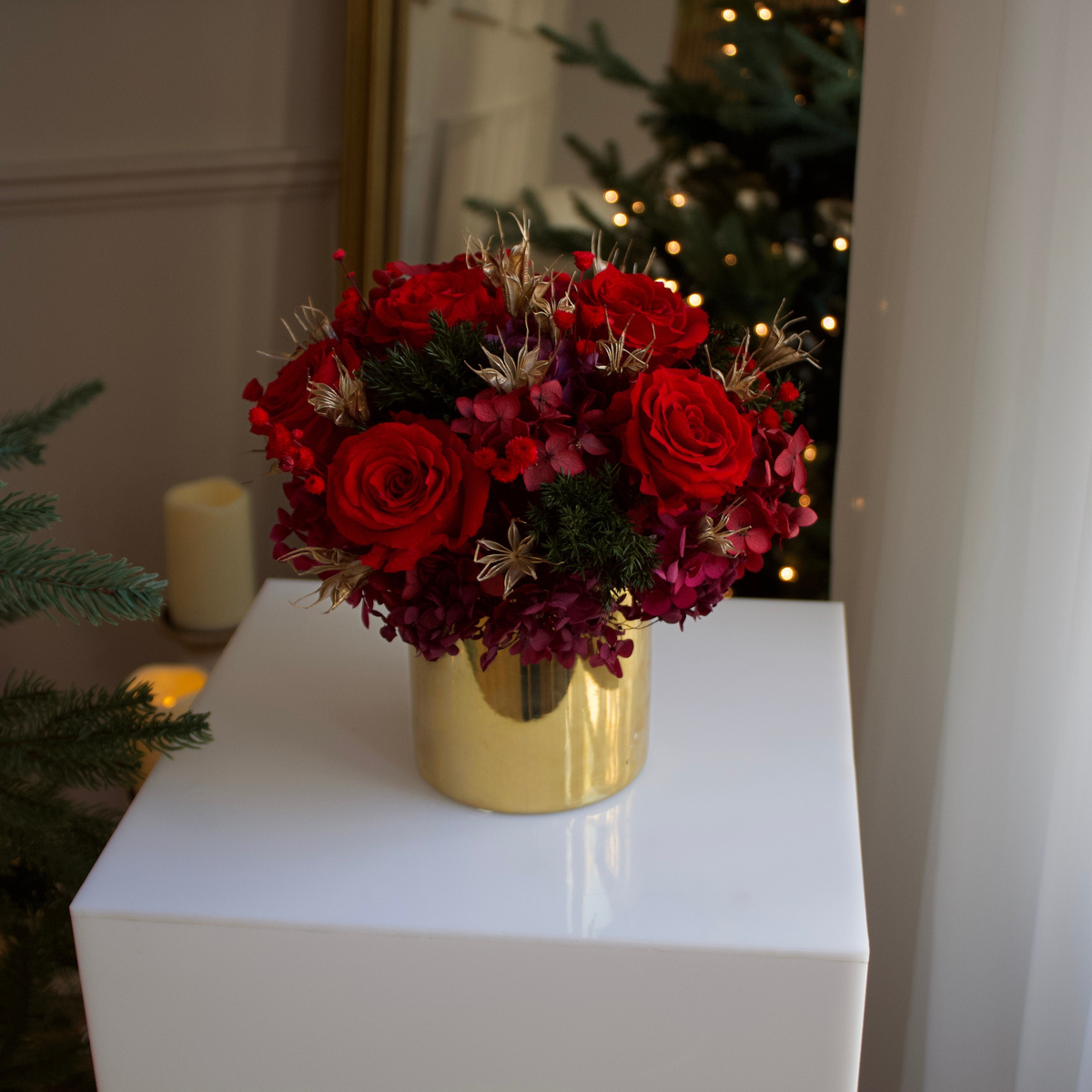 The Jubilee (Petite) by Eos Blooms rests on a pedestal near a lit Christmas tree.