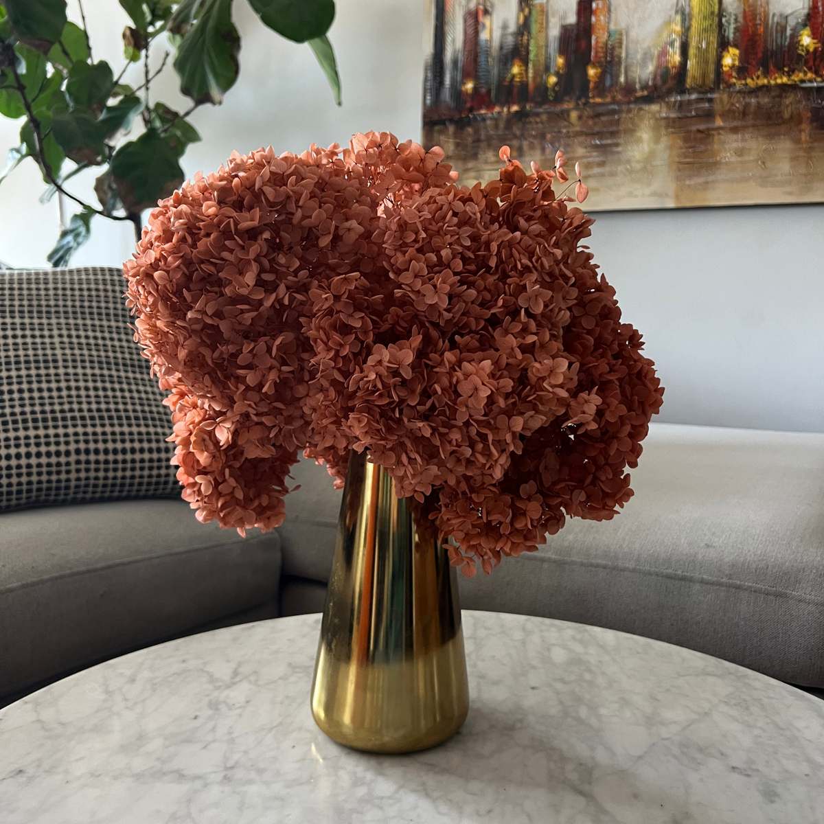 Eos Blooms Preserved Hydrangeas in a gold vase on a round marble table in a modern room.
