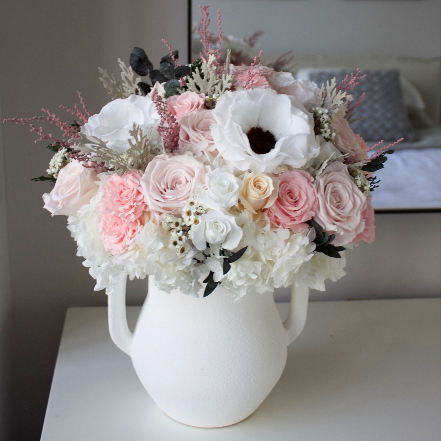 The Gossamer by Eos Blooms: preserved pastel florals in a white vase on a bedroom table.