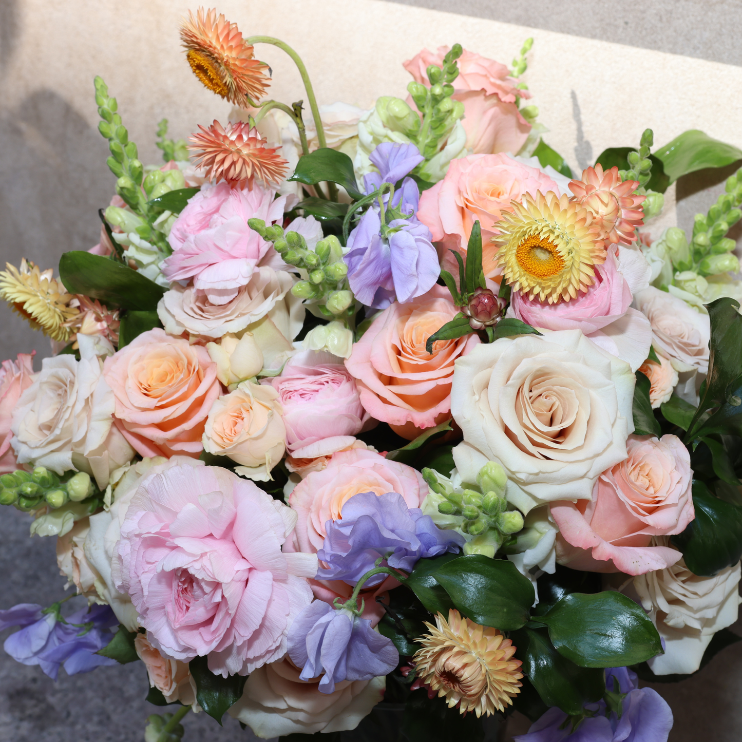 The Highnoon by Eos Blooms: apricot roses & purple blooms in a pastel arrangement.