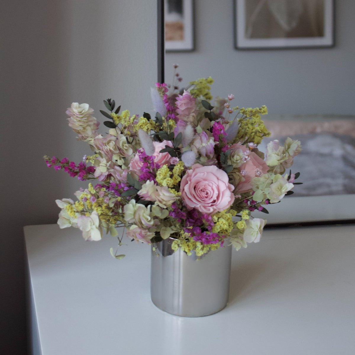 The Avonlea (Petite) by Eos Blooms: pastel preserved roses in a silver vase by a mirror.
