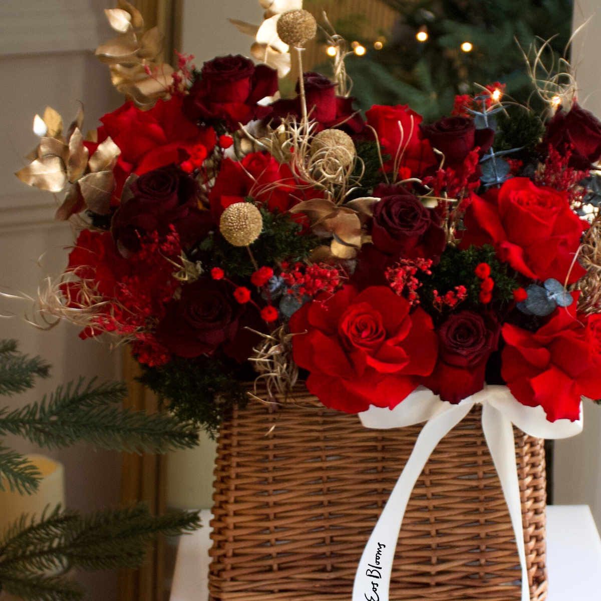 The Fireside Holiday Basket by Eos Blooms features red roses, gold accents, and a white ribbon.