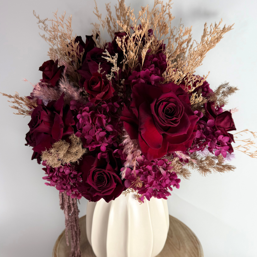 Bouquet of red and purple flowers in a white vase on a wooden surface with a white background