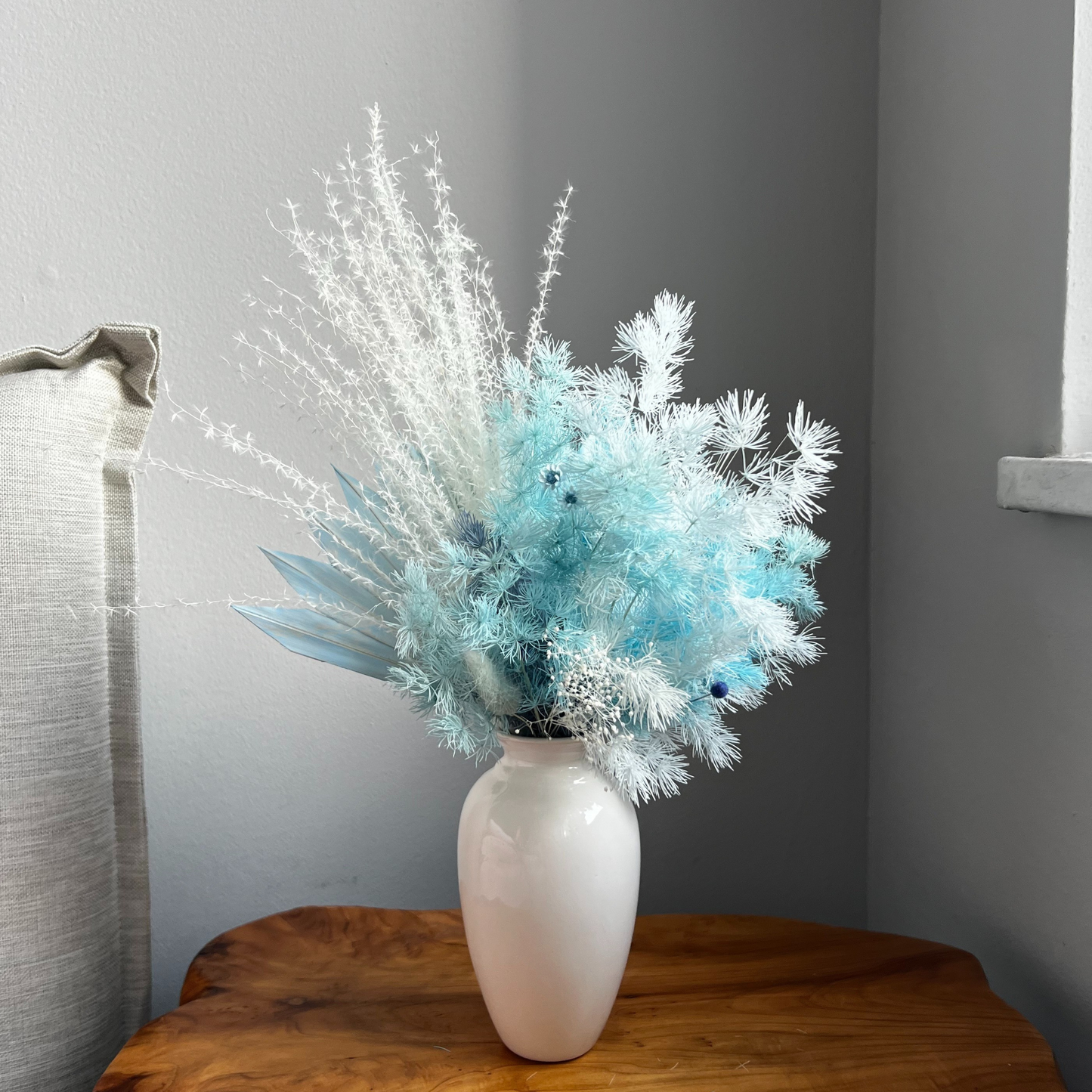 Serenity by Eos Blooms: elegant white vase with Forever Roses on a table by a gray wall.