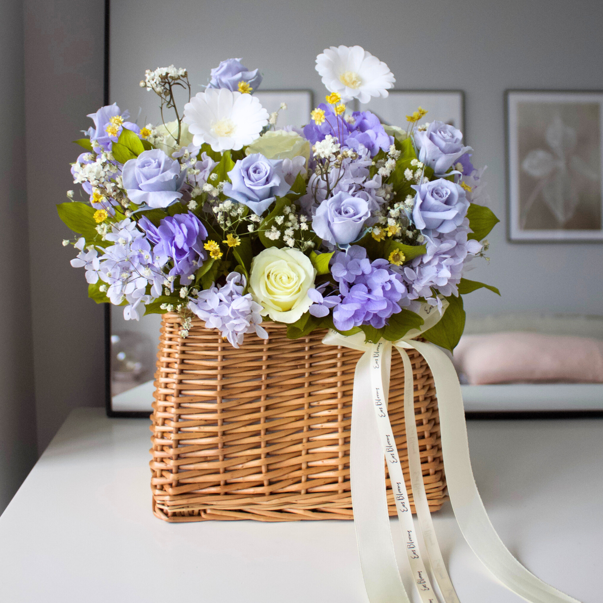 The Revival | Spring Basket by Eos Blooms with purple, white, yellow blooms on a white table.