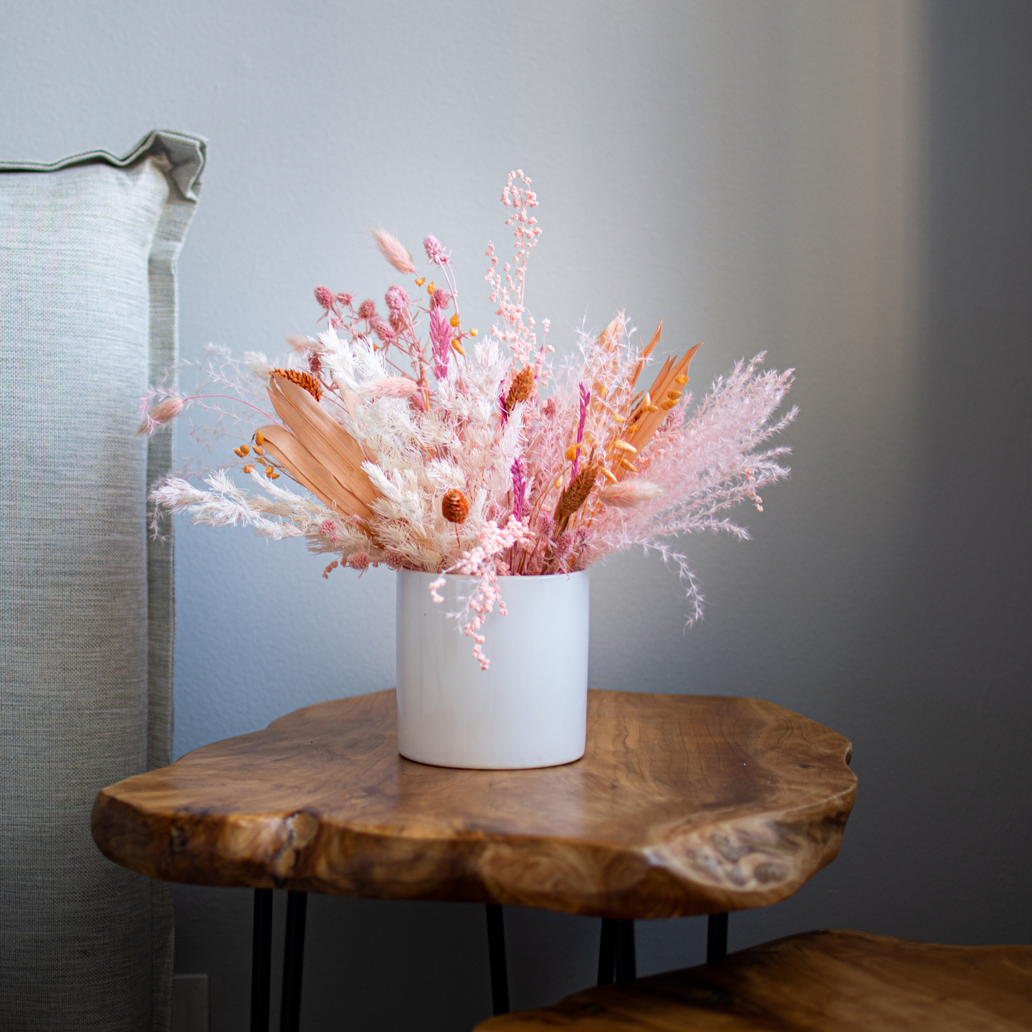 The Dune vase by Eos Blooms with Forever Flowers sits on a wood table by a gray cushion.