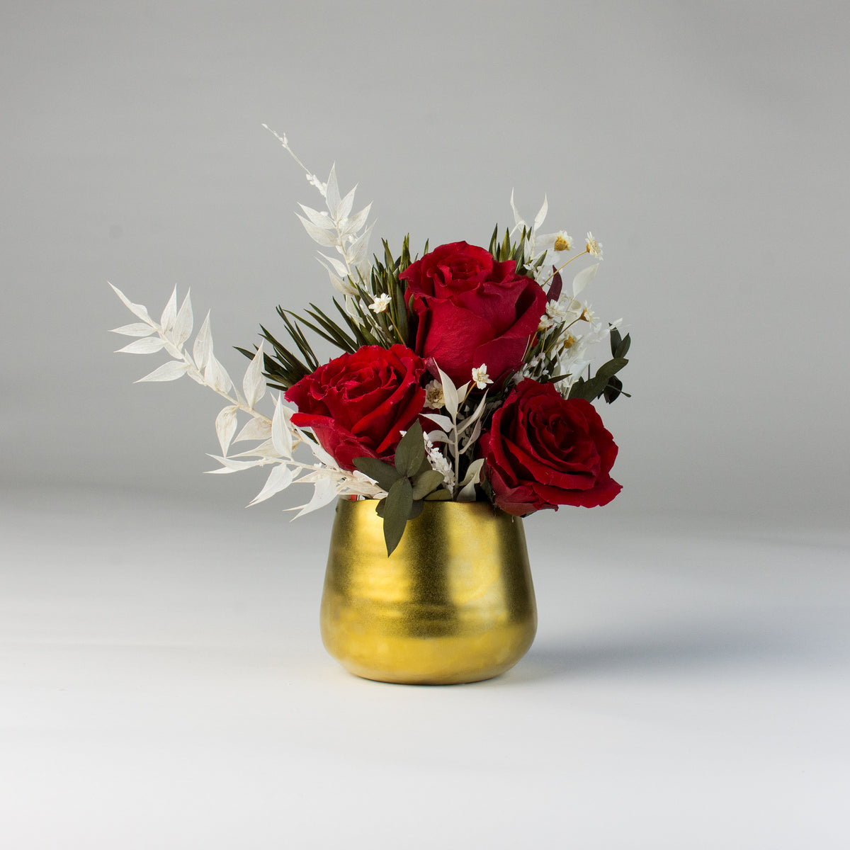 Eos Blooms Mini: Forever Roses with white foliage in a small gold vase for lasting beauty.