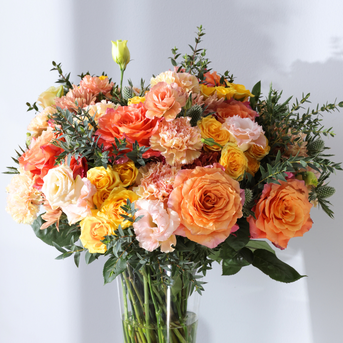Bouquet of orange, yellow, and peach roses and carnations in a glass vase.