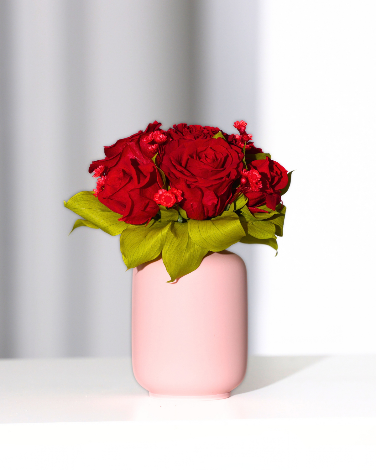 Eos Blooms Mini Milk Jars in a pink vase with green leaves on white, light background.
