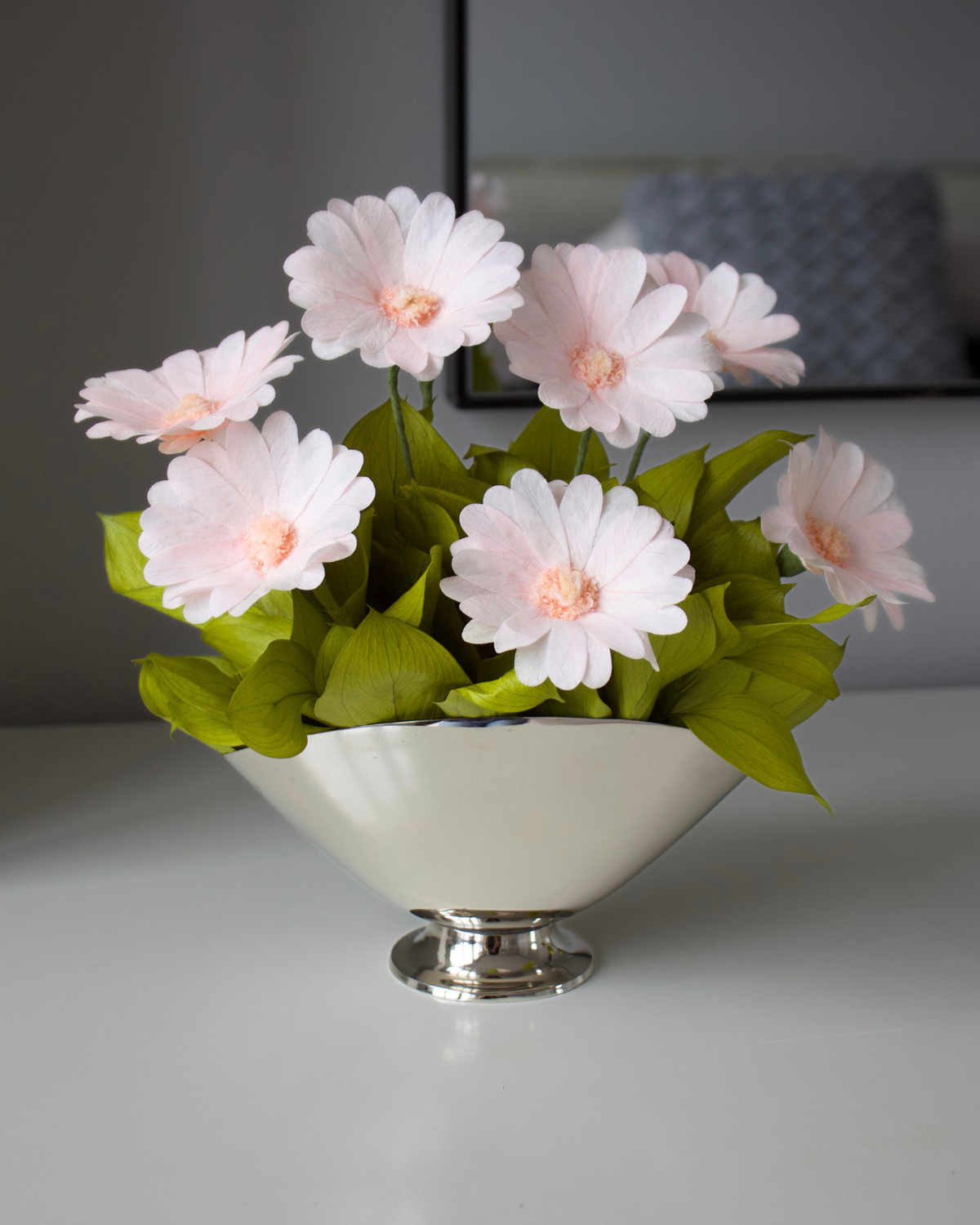 The Margarita by Eos Blooms: preserved daisies in silver vase, light pink blooms, green leaves.