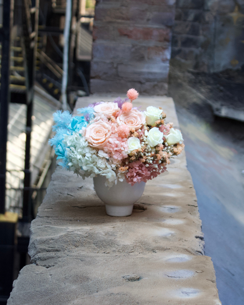 The Aquarella (Petite) by Eos Blooms: pastel preserved florals in a white vase on a stone ledge.