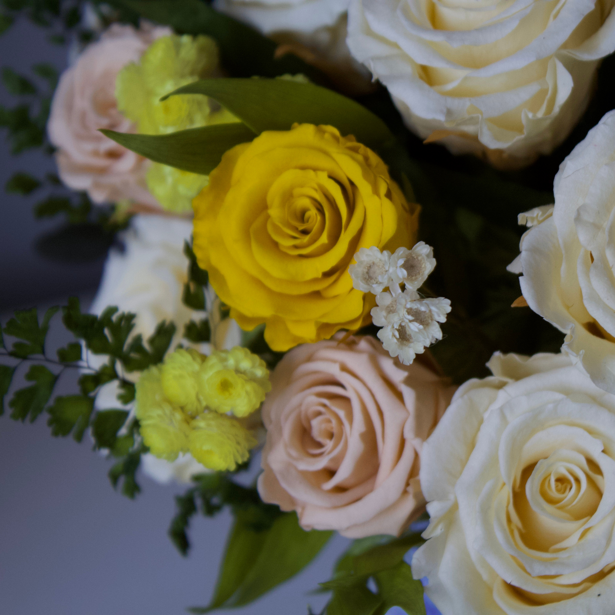 Bouquet of yellow and white roses with greenery and small white flowers.