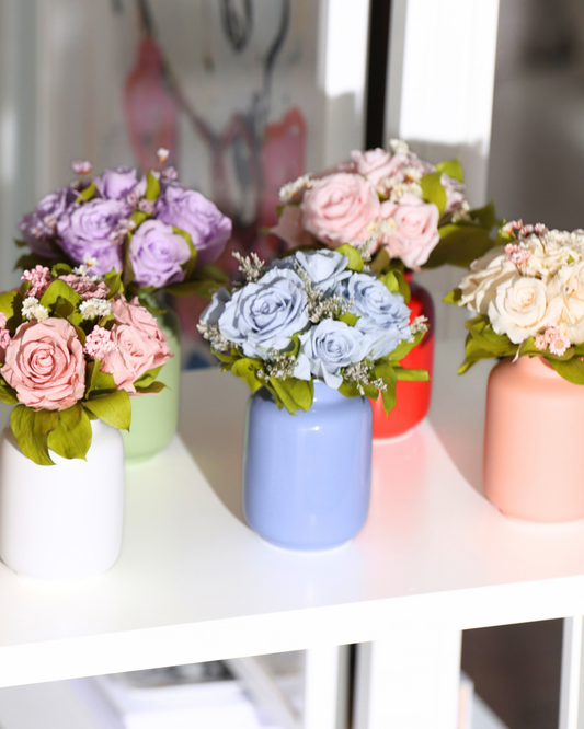 Five Eos Blooms Mini Milk Jars with Forever Roses sit on a white shelf in bright light.