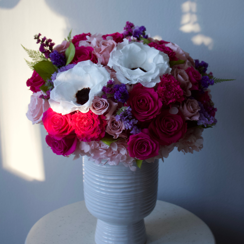 The Zenith by Eos Blooms: pink, purple, and white flowers in a ribbed vase on a round table.