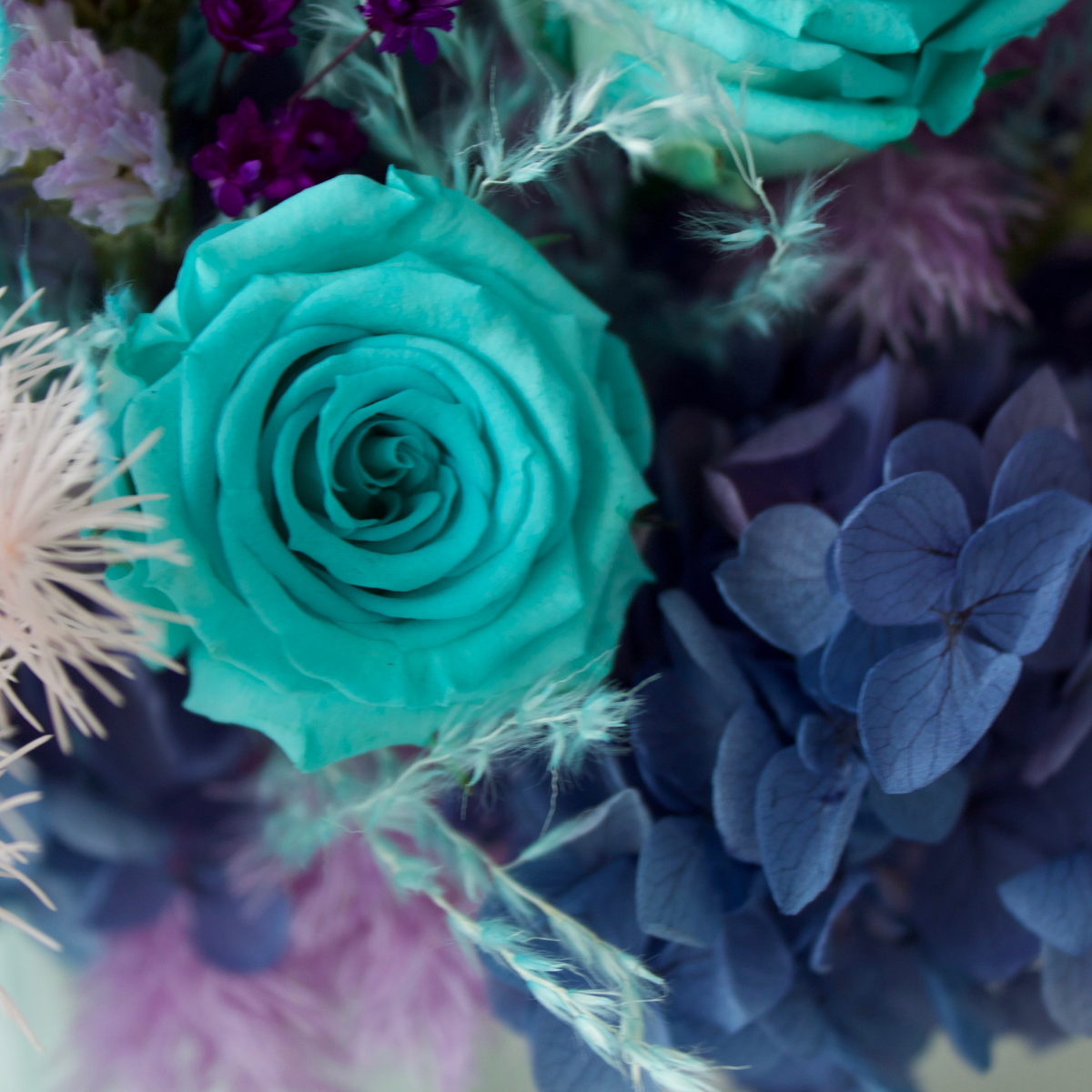 La Sirena by Eos Blooms: Turquoise rose, blue hydrangea, and feathers in a preserved arrangement.