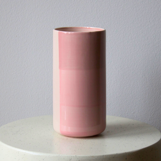 The Blush Vase by Eos Blooms shines on a white surface with a gray wall in the background.