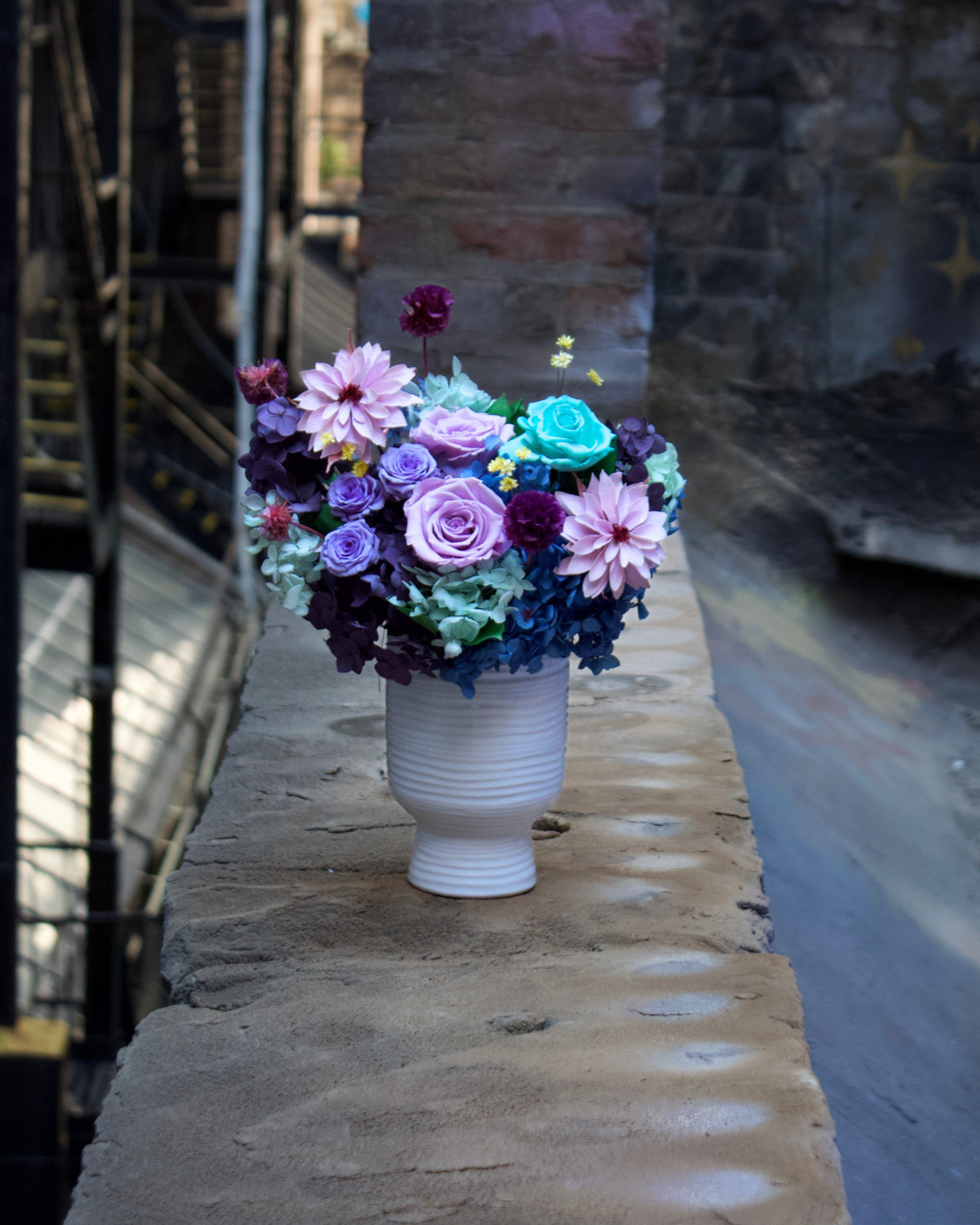 The Jewel Box (Petite) by Eos Blooms rests on a stone ledge in an urban alleyway.