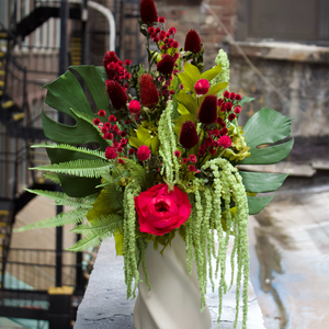 Floral arrangement with red and green flowers in a white vase on a concrete surface.