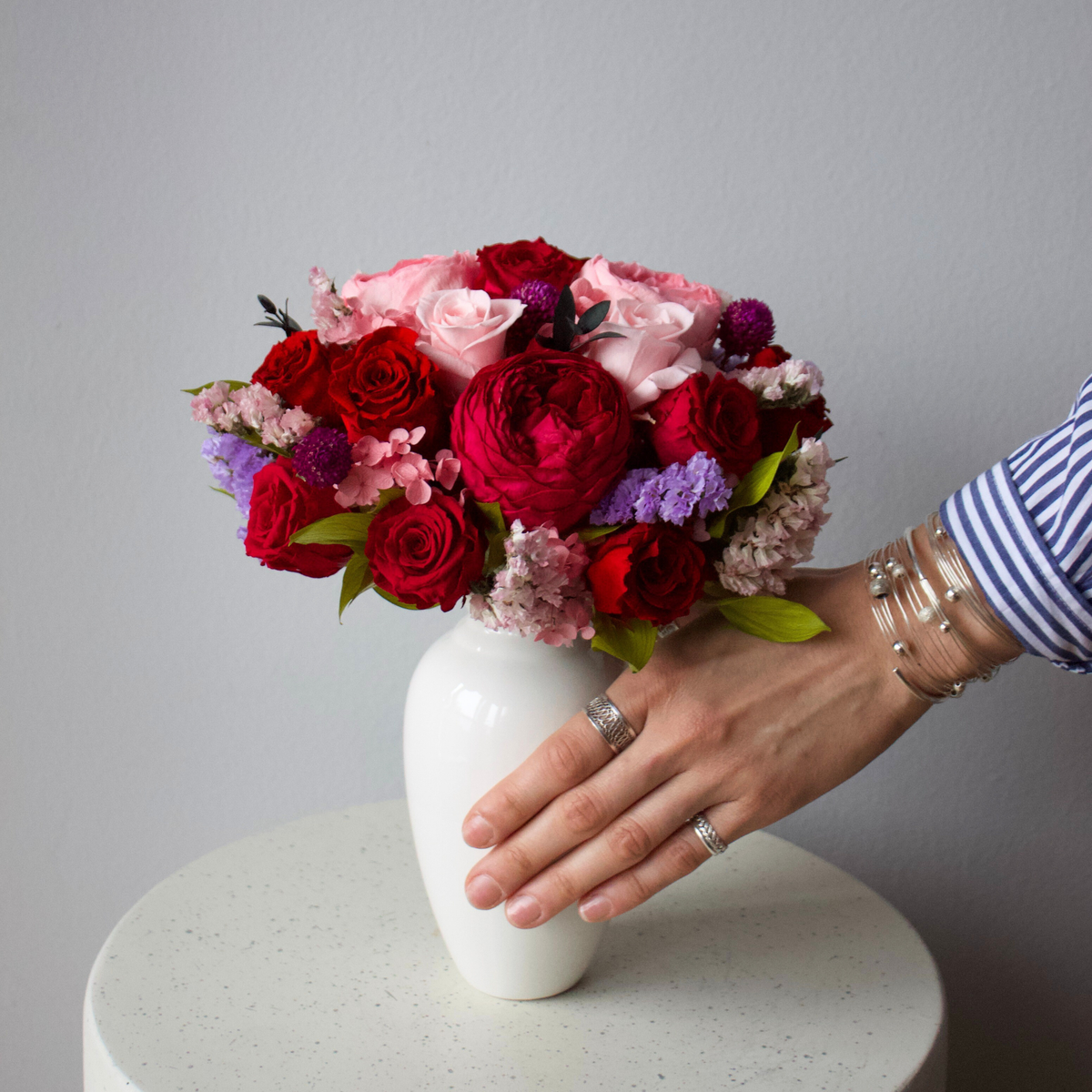 Ma Chérie (Petite) by Eos Blooms arranged by hand on a white table against a gray wall.