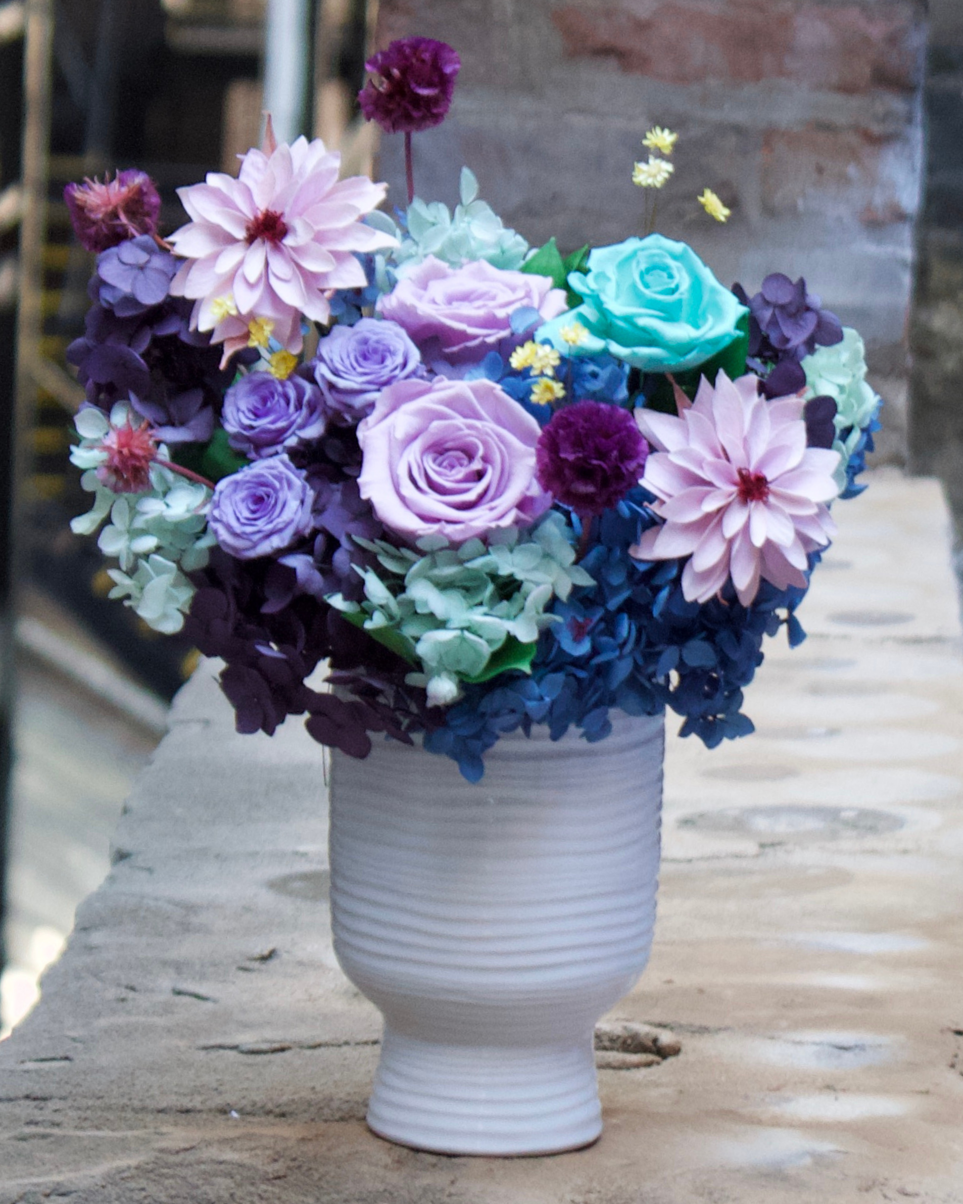 The Jewel Box (Petite) by Eos Blooms: purple, pink, and blue blooms in a white vase.