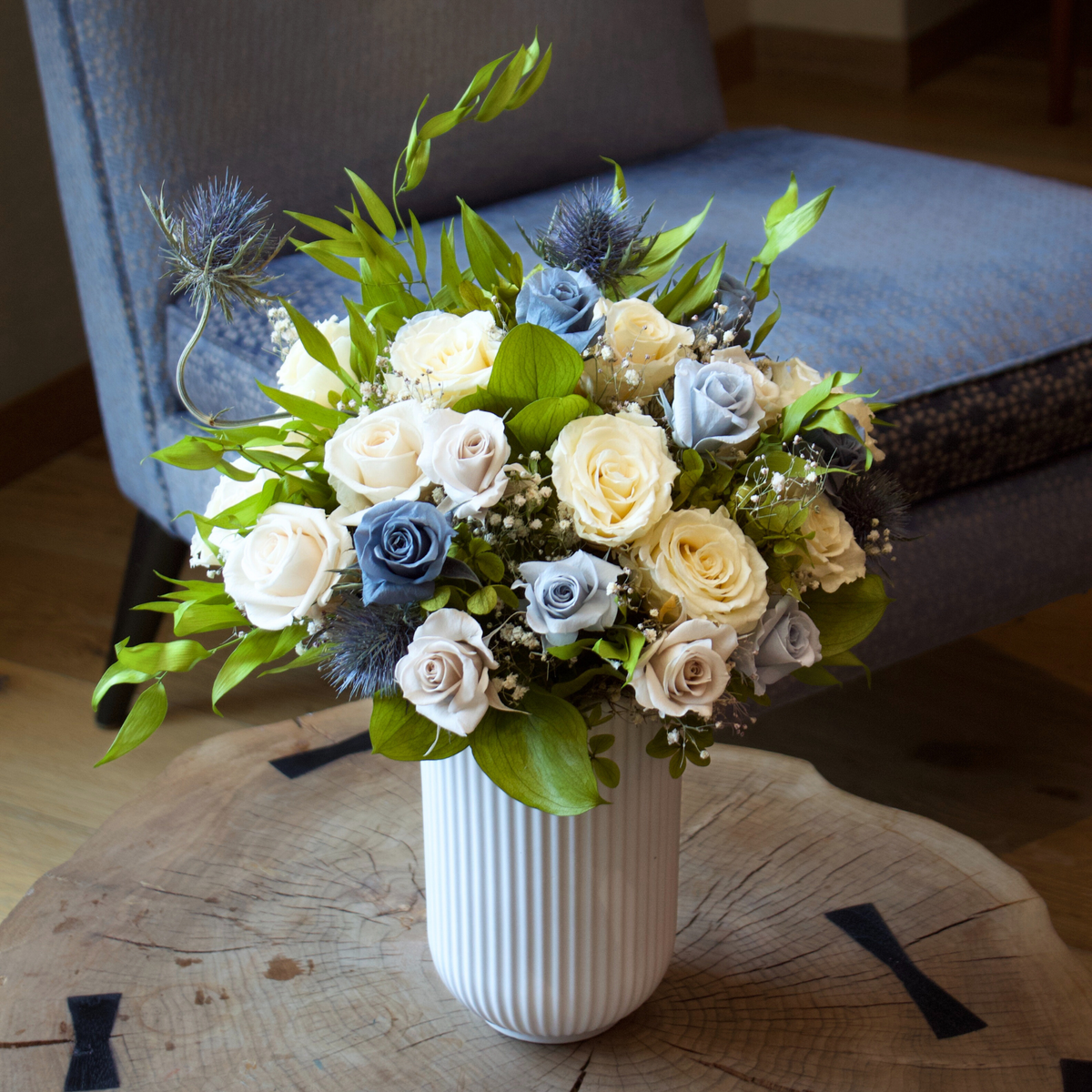 The Nantucket by Eos Blooms: preserved cream and blue roses in a vase on a wooden table.