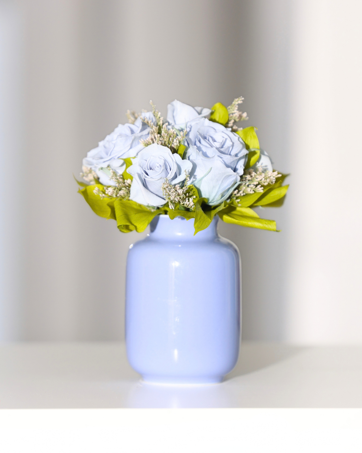 Blue Forever Roses & greenery in Eos Blooms Mini Milk Jar, displayed on white surface.