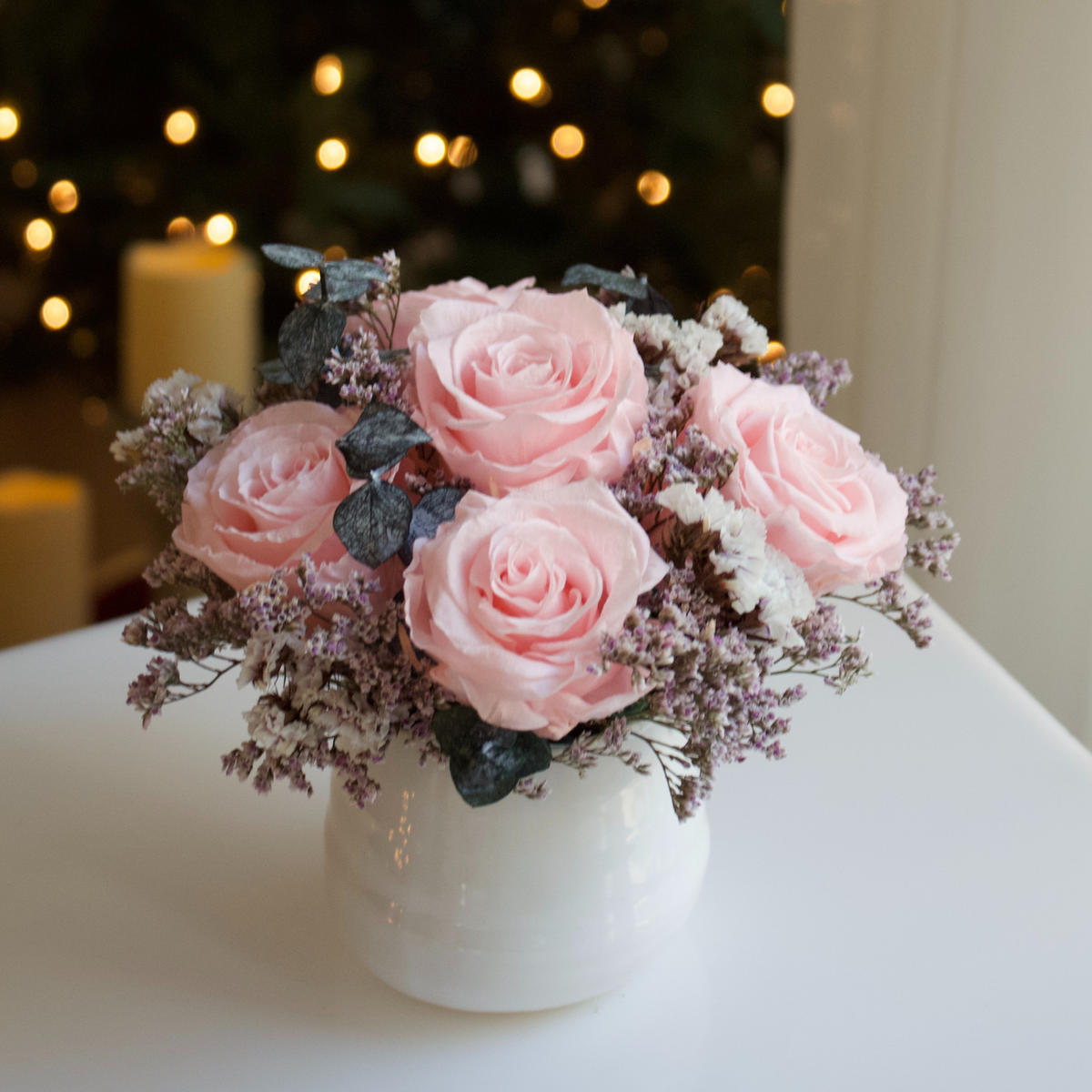 Eos Blooms Mini: Pink Forever Roses & white blooms in a white vase with glowing lights behind.