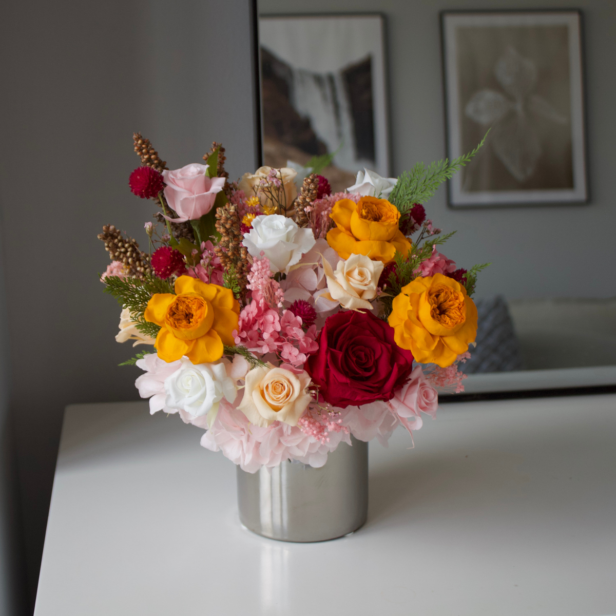 The Reverie (Petite) by Eos Blooms: preserved flowers in a silver vase on a white table.
