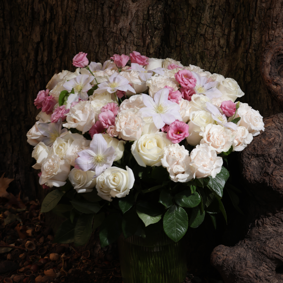 The XOXO by Eos Blooms: white and pink flowers with green leaves beside a tree trunk.