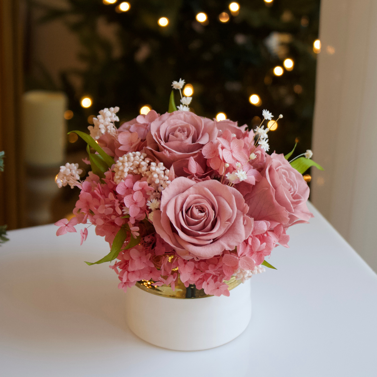 Eos Blooms' Mini: a white vase with preserved flowers and pink roses, softly glowing.