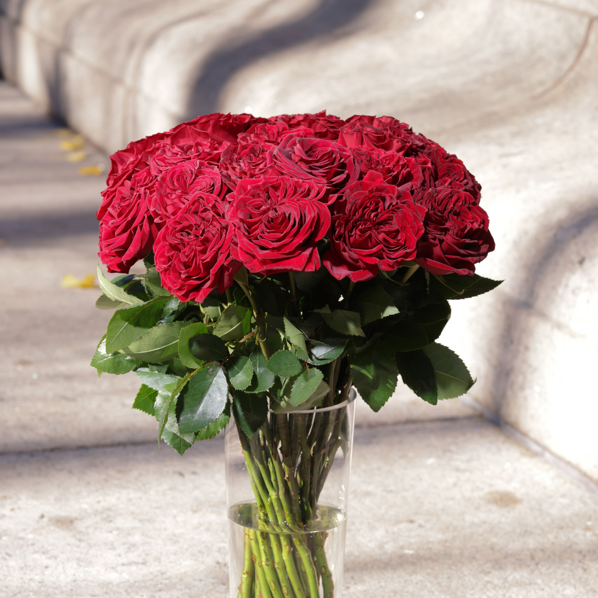 Mon Coeur by Eos Blooms: lush Hearts roses in a clear glass vase on stone steps.