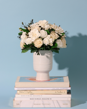 The Snowdrop by Eos Blooms: preserved roses in a vase sit on books, blue backdrop.