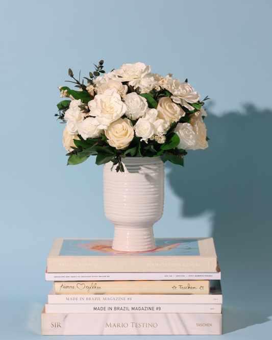 The Snowdrop by Eos Blooms: preserved roses in a vase sit on books, blue backdrop.