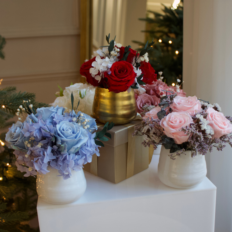 Four flower arrangements in pastel and red colors in white and gold vases on a white pedestal.