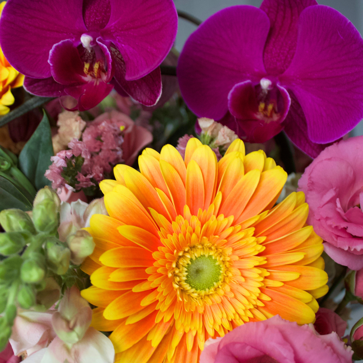 Bright yellow daisy with pink flowers and purple orchids in a colorful bouquet.