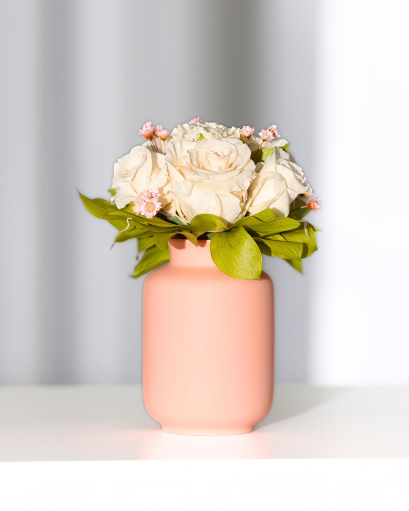 Mini Milk Jar by Eos Blooms with Forever Roses, pink flowers, and green leaves on white surface.