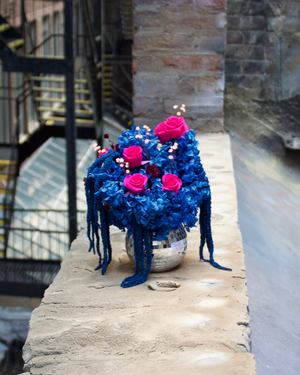 Studio 54 (Petite) by Eos Blooms: preserved roses & blues in glass vase on a brick ledge outside.