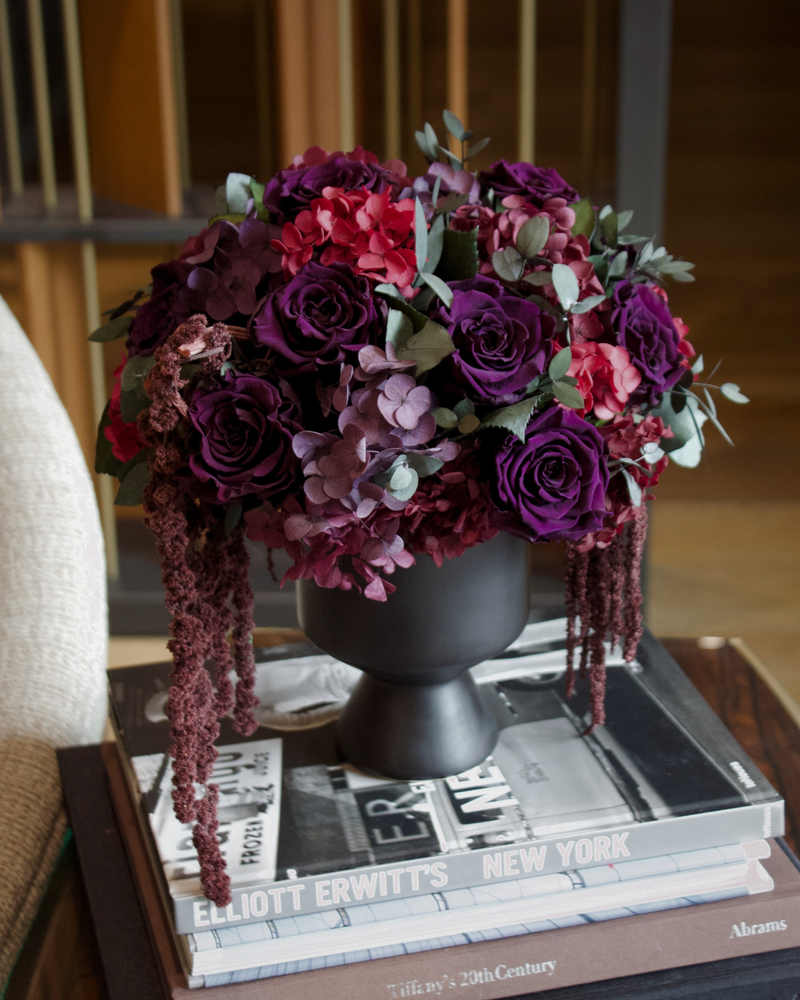 After Hours by Eos Blooms: purple and red preserved florals in a black vase on stacked books.
