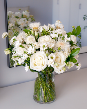 The Blanche by Eos Blooms, ivory roses arranged elegantly on a white table near a mirror.