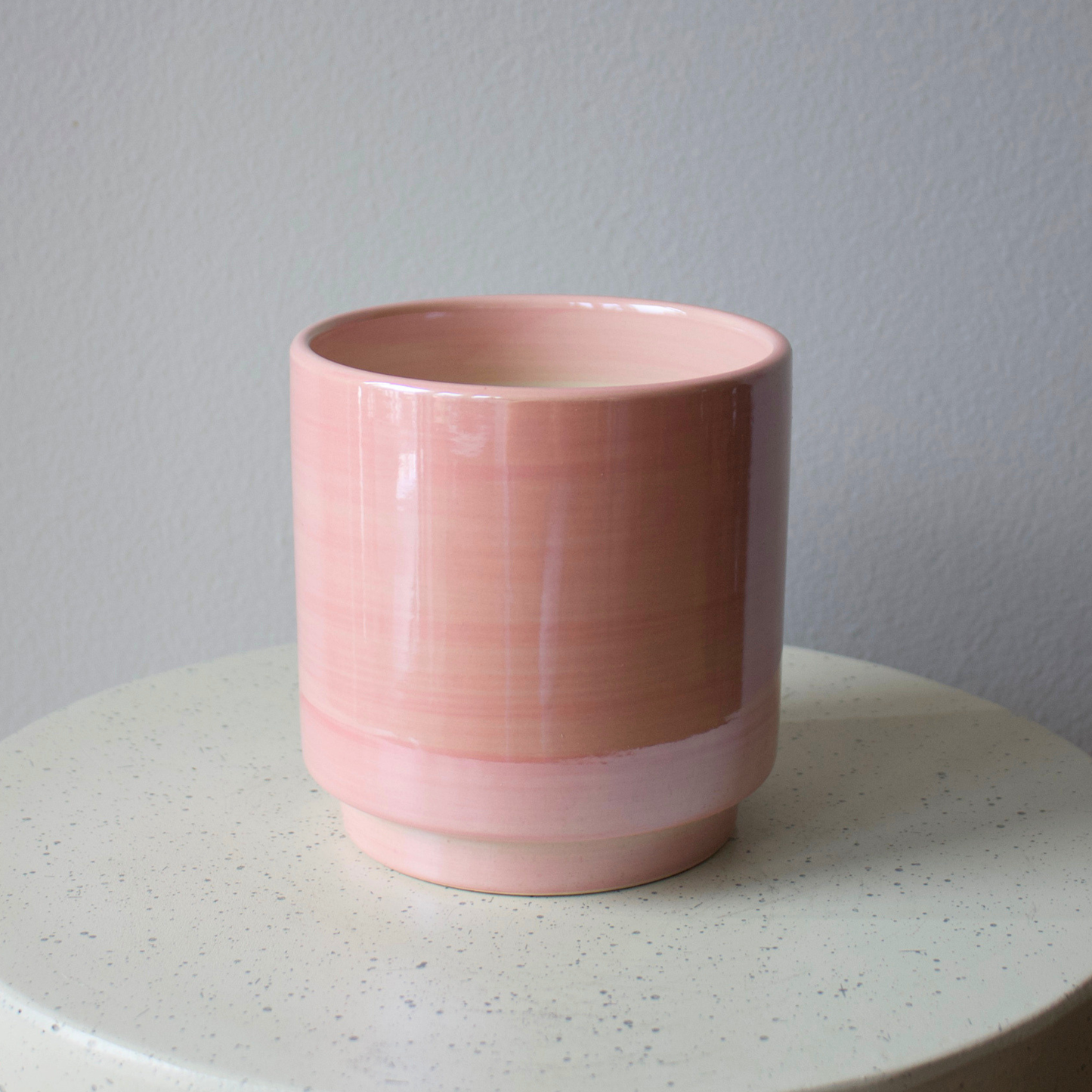 The pink Dawn Vase by Eos Blooms rests on a white speckled round surface, gray wall behind.