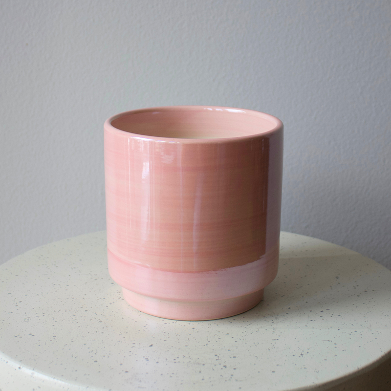 The pink Dawn Vase by Eos Blooms rests on a white speckled round surface, gray wall behind.