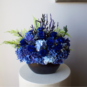Bouquet of blue and purple flowers in a black vase on a white surface with a light gray wall background.