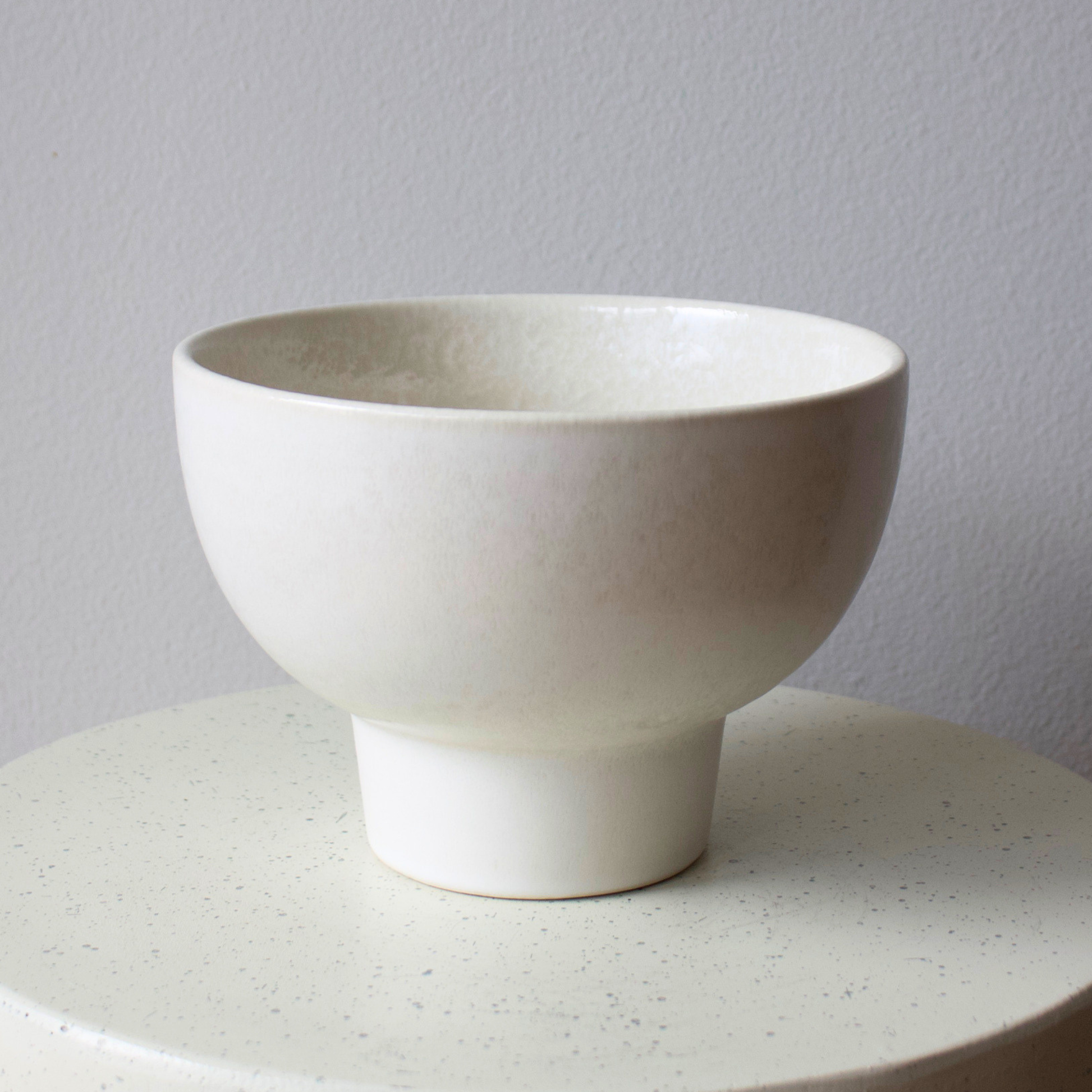 The Eos Blooms White Ceramic Pedestal (Medium) rests on a round, light-colored surface.
